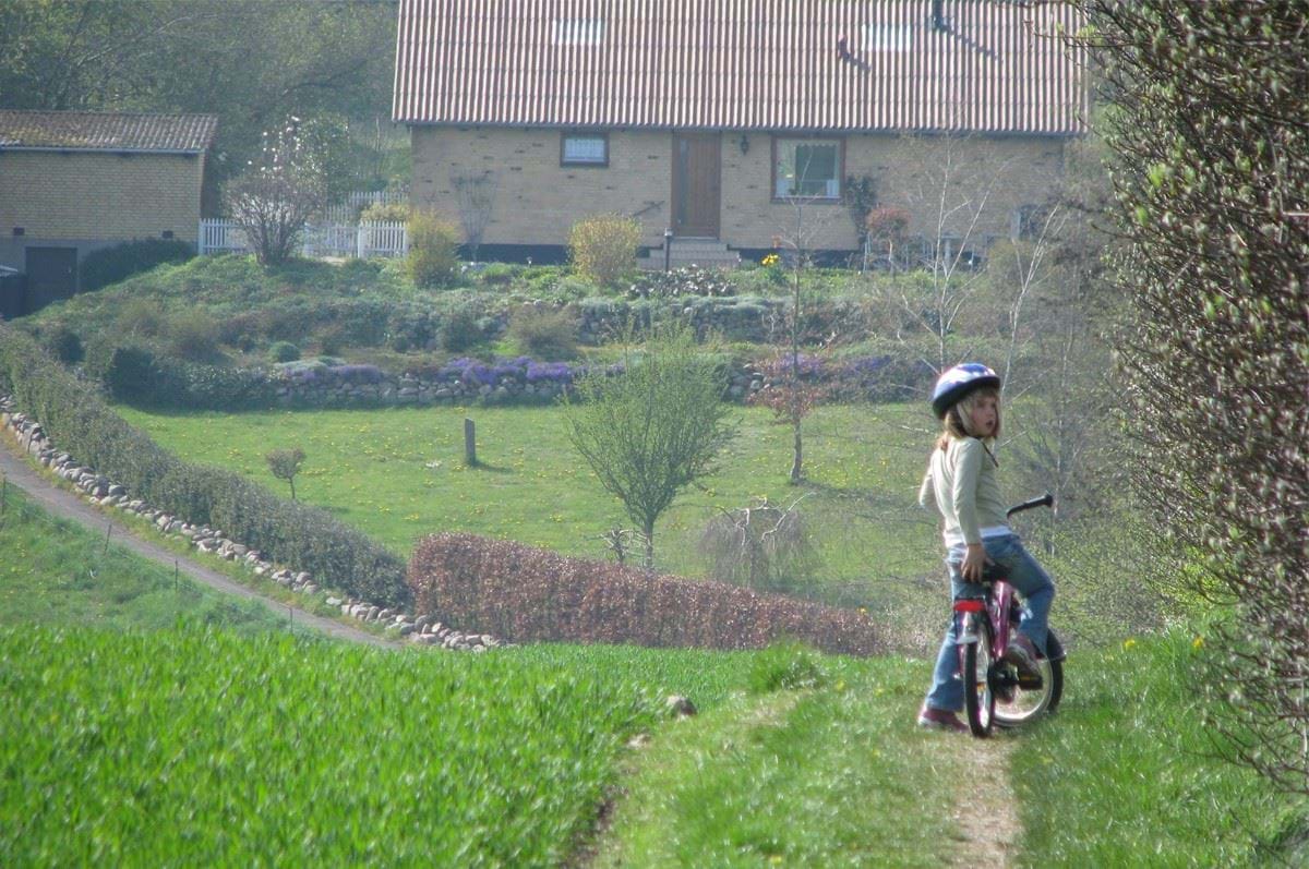 Lille pige på cykel står på en sti ved læhegn
